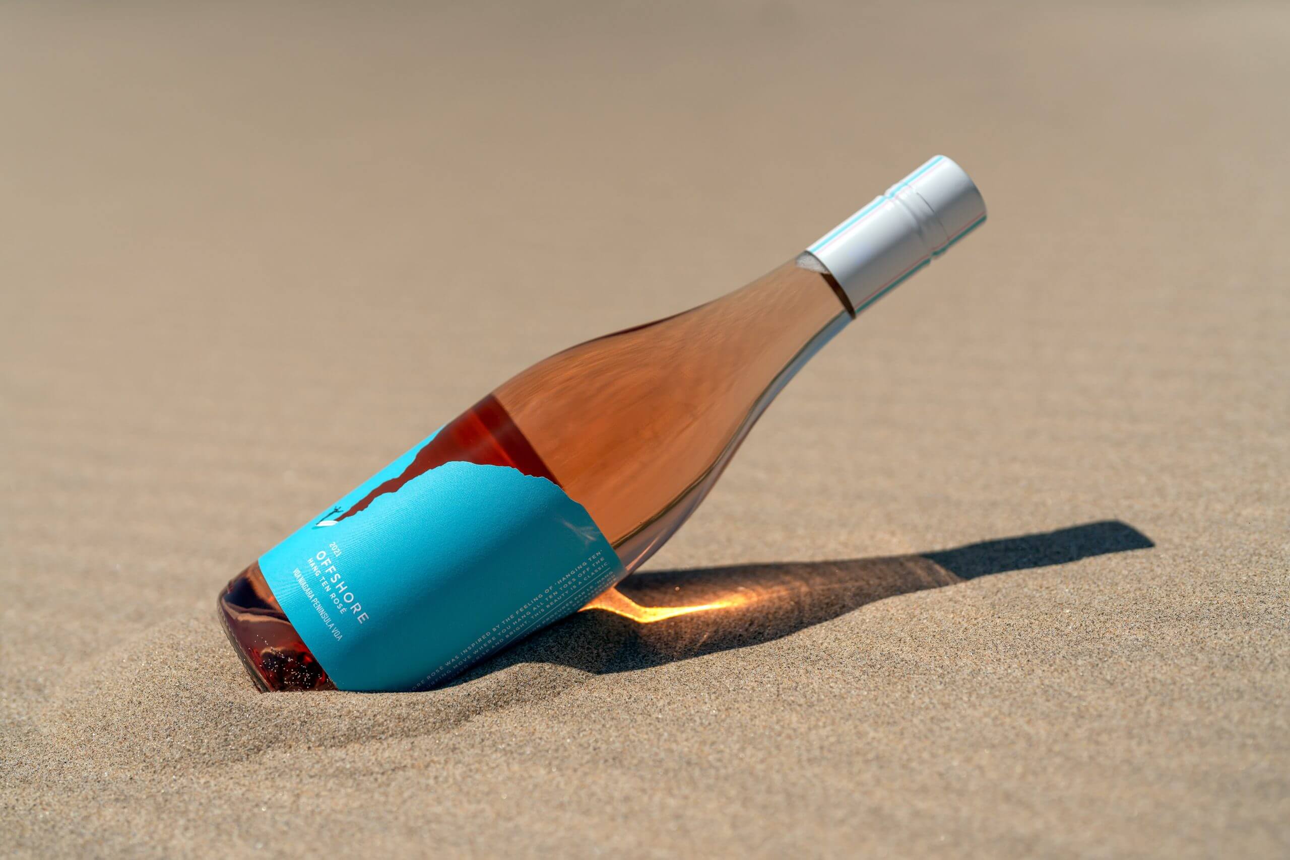 A bottle of rose wine sits in the sand