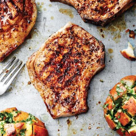 Grilled pork chops arranged on a pan with bread and a fork.