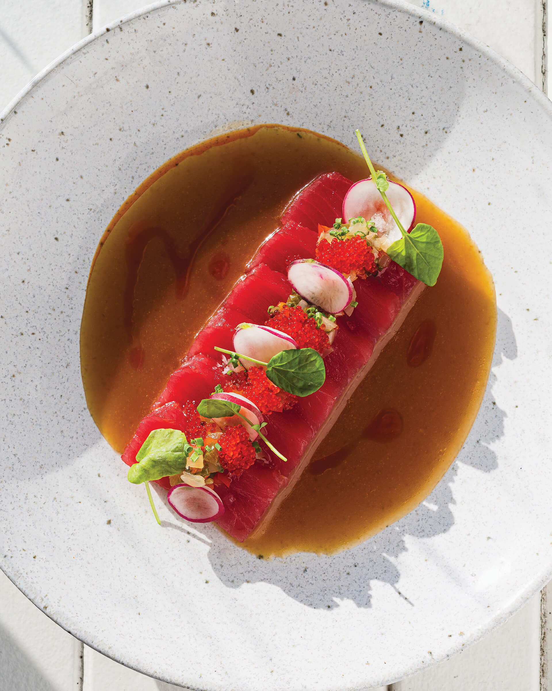 Bright red tuna crudo on a white dish.