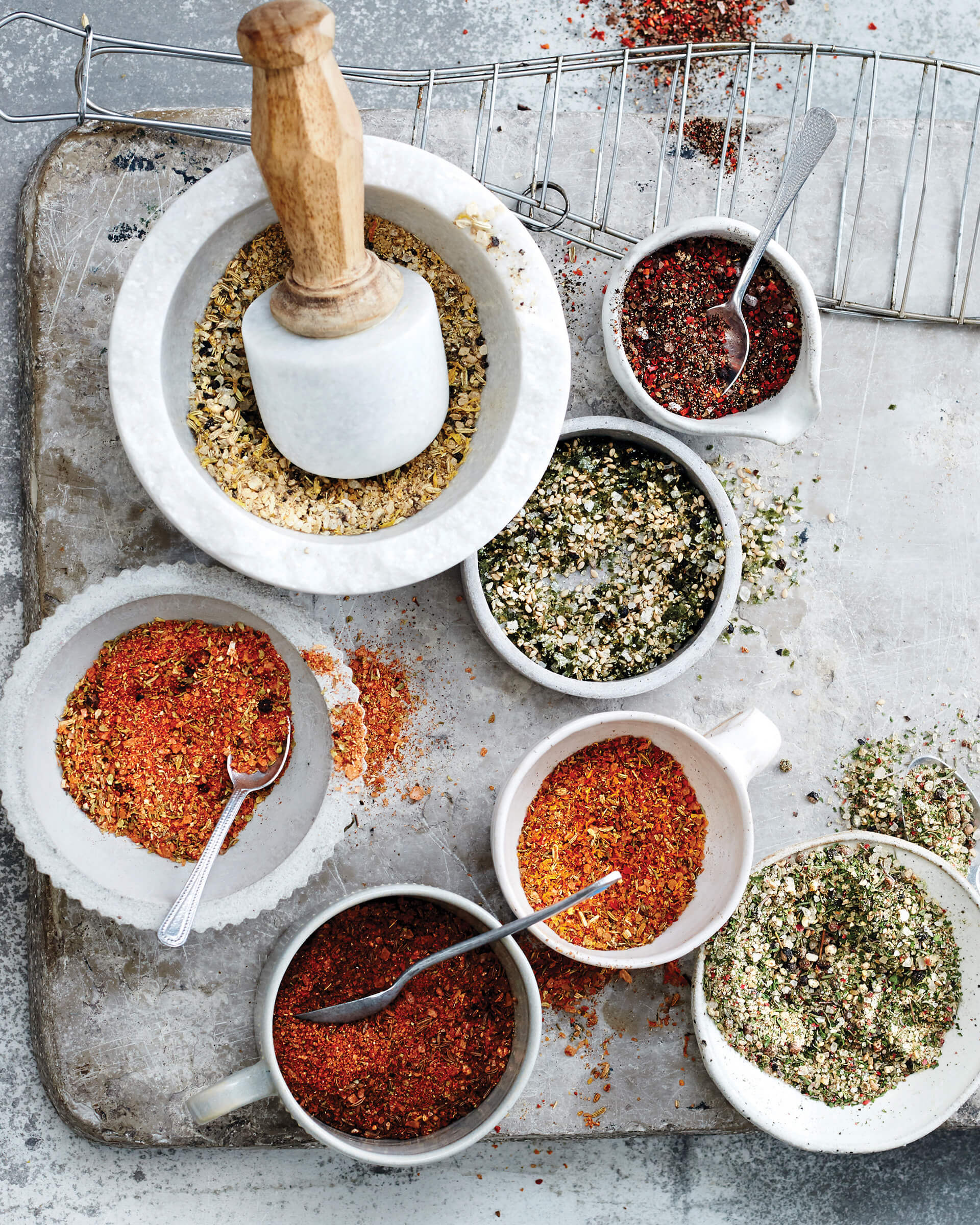 Bowls of mixed spices next to a white mortar and pestle