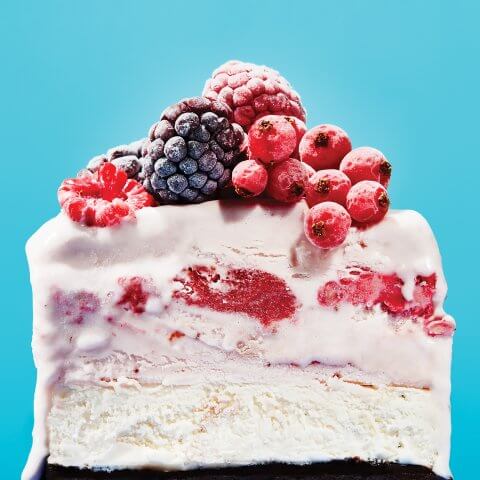 A vanilla ice cream cake with mixed berries against a bright blue backdrop.