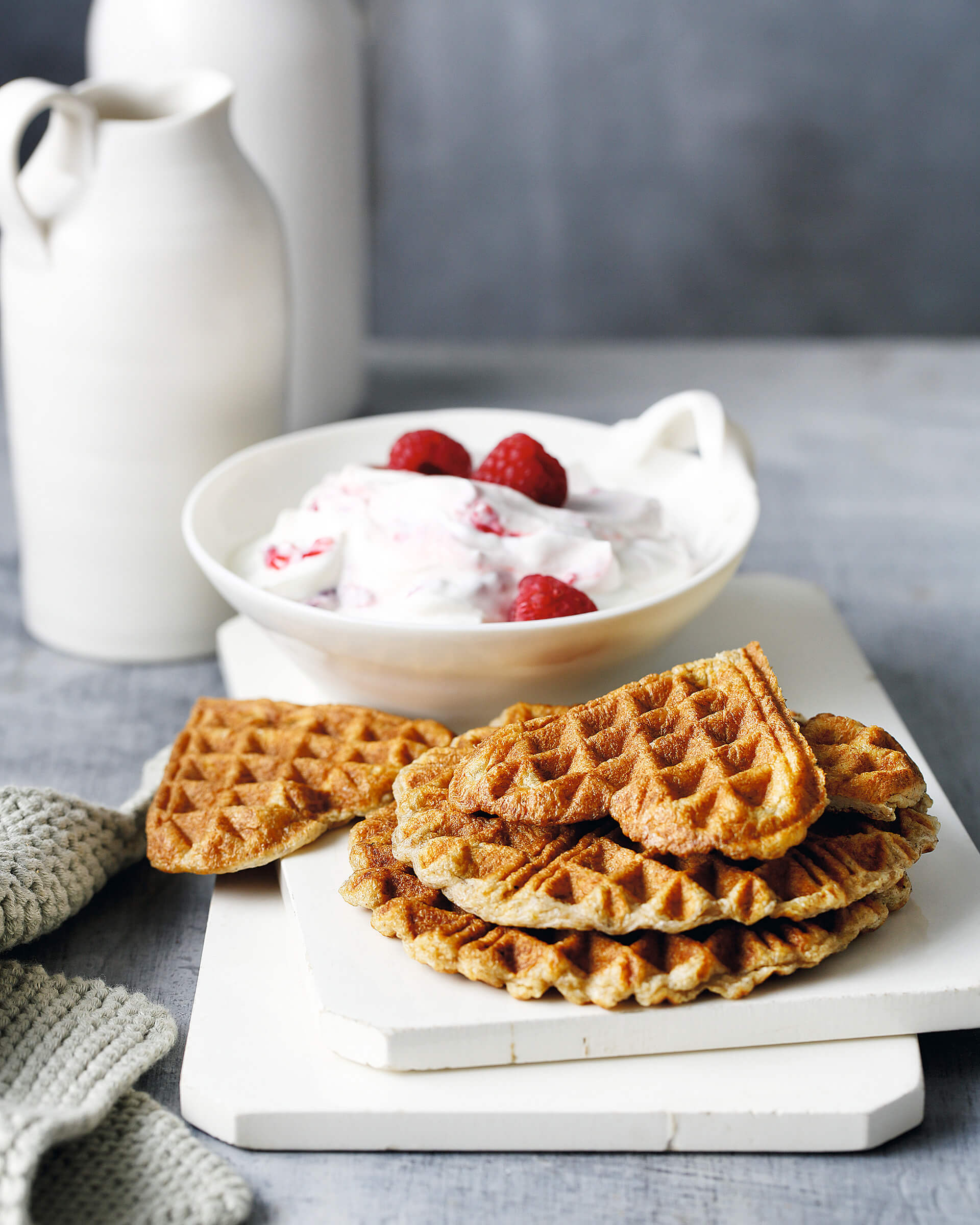 A heart-shaped waffle on top of a stack with yoghurt and fruit in the background.
