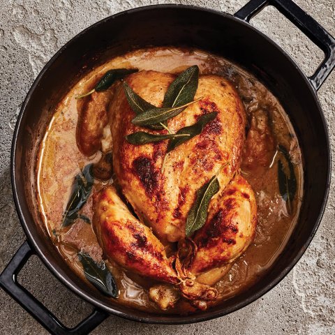 A cast iron pot with a whole chicken covered in herbs and sauce