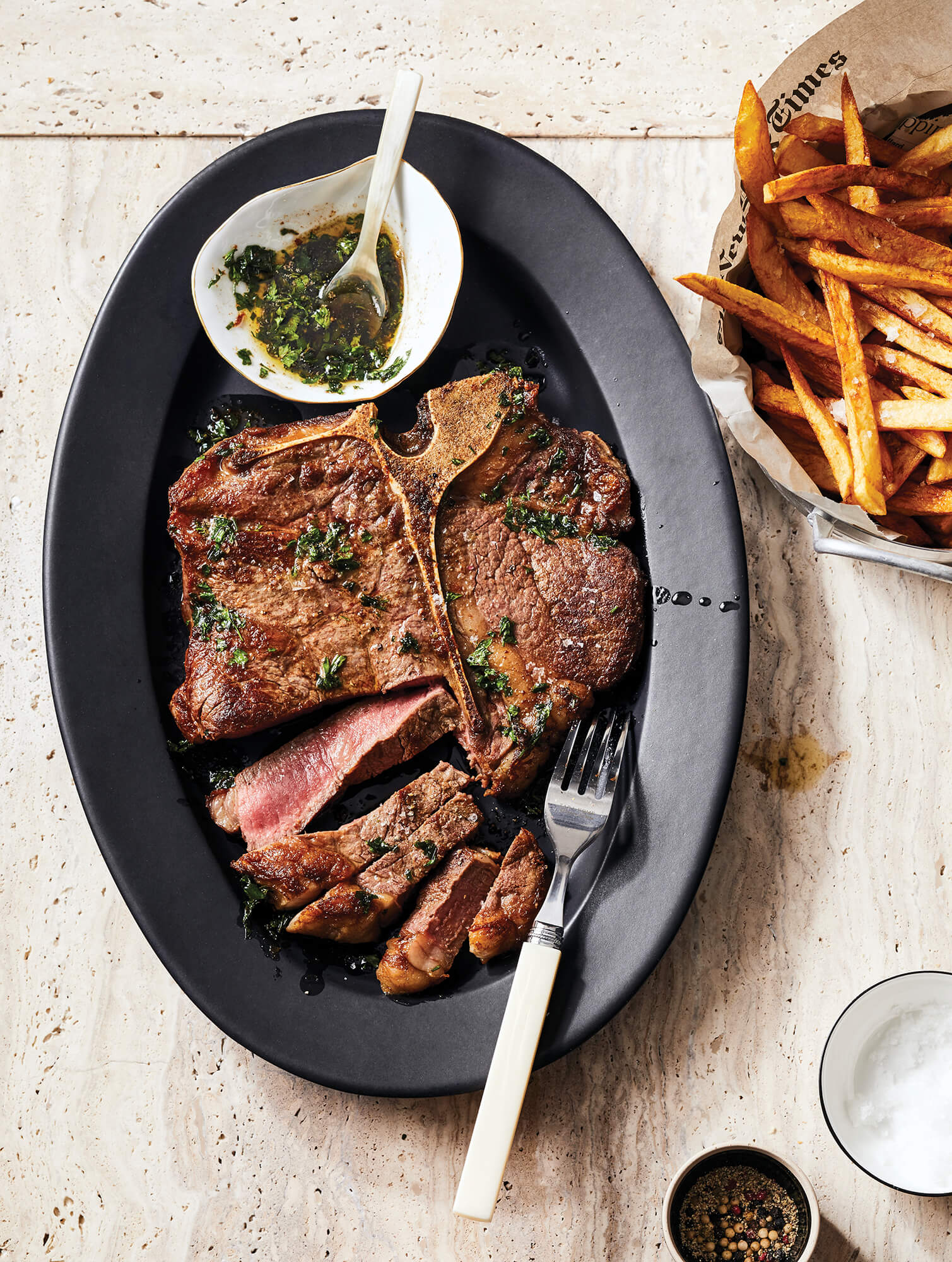 A sliced steak on a black plate with fries and sauce on the side.