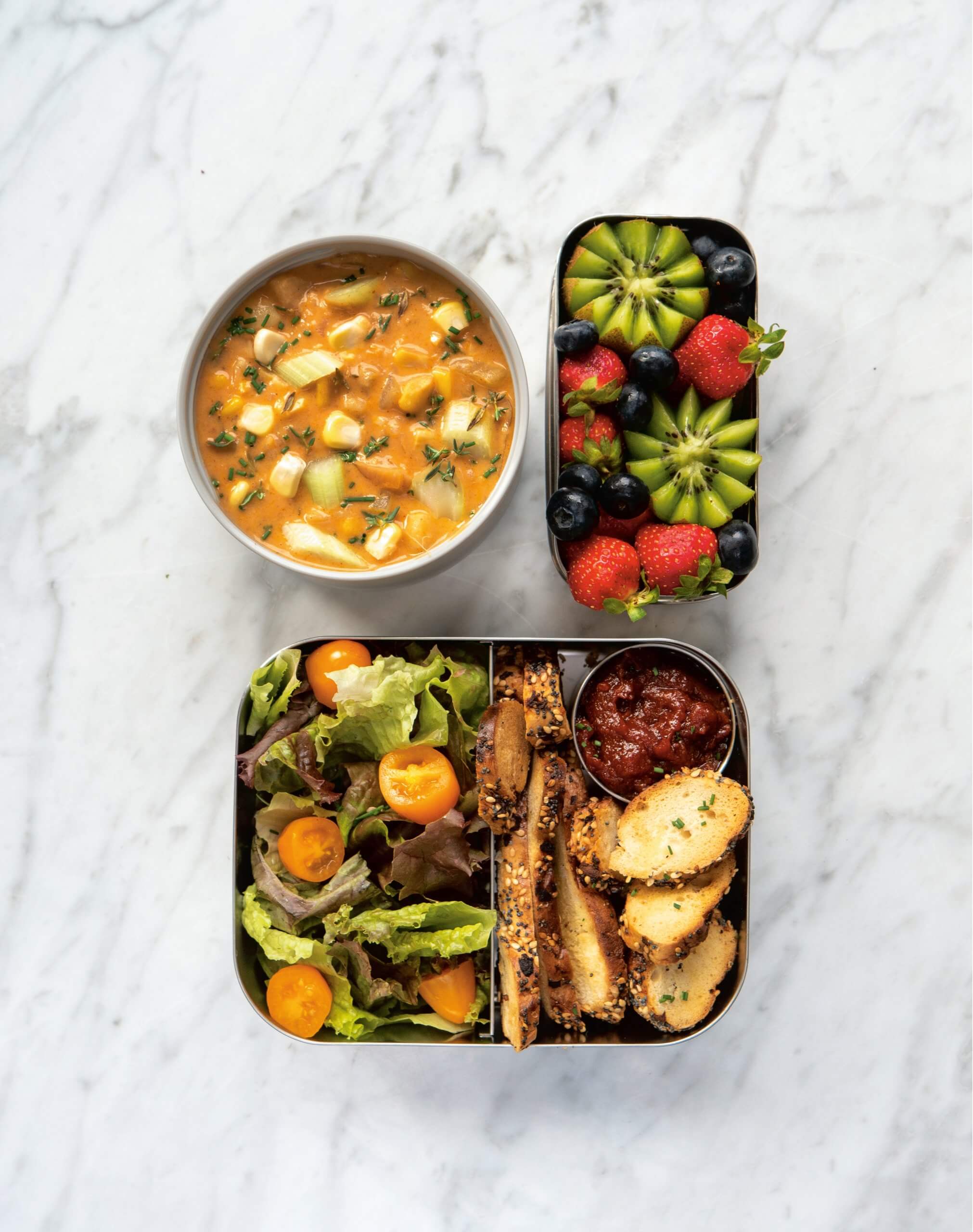 Three tin containers with soup, salad and fruit.