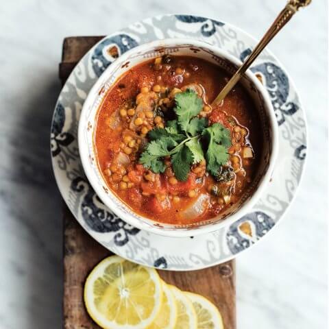 A bowl of red lentil soup with sliced lemons next to it