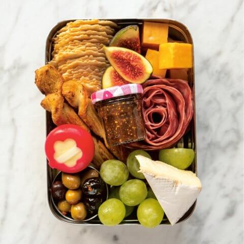 A tin lunchbox with a little jam jar and assorted snacks.
