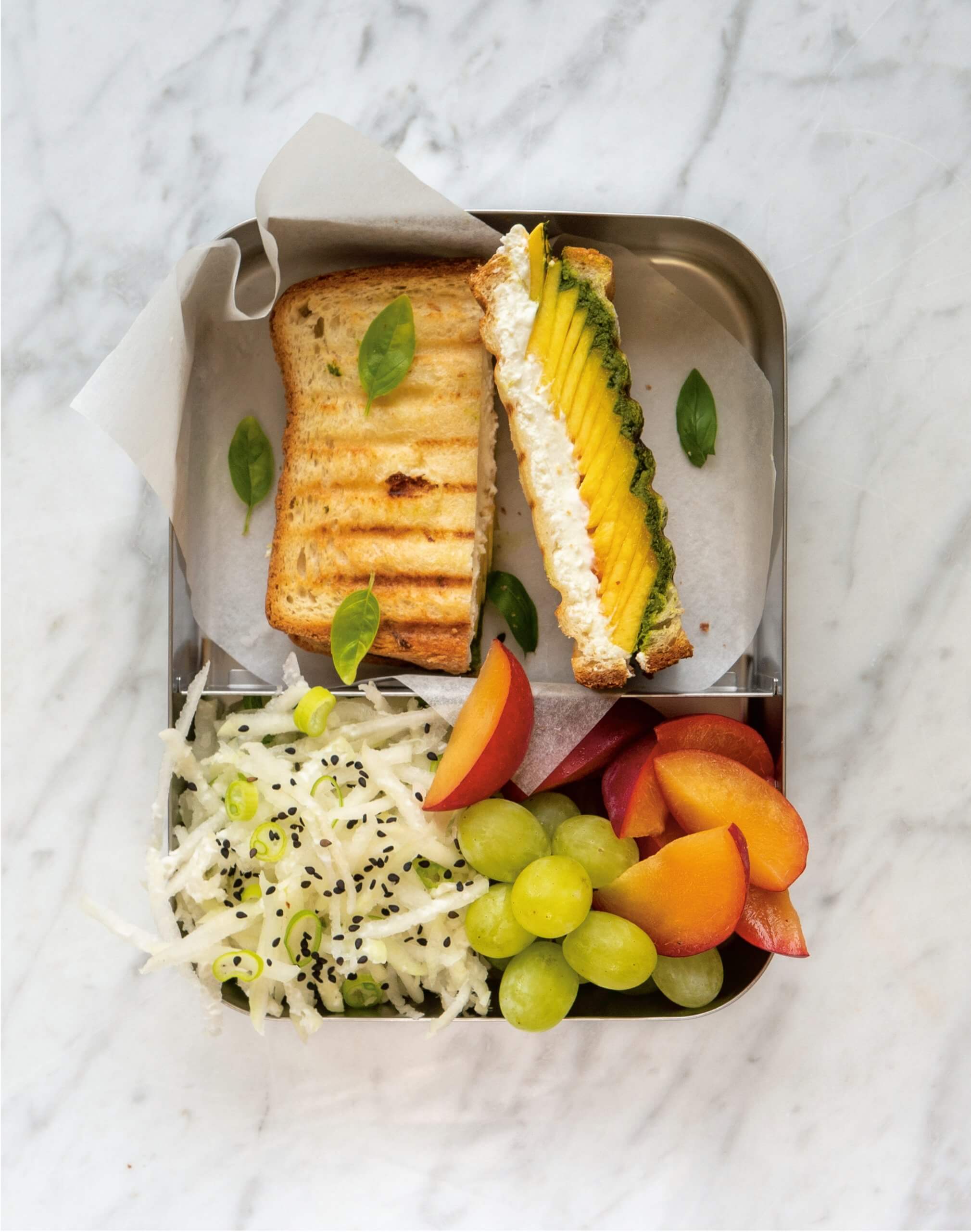 A sliced sandwich with fruit in a tin box