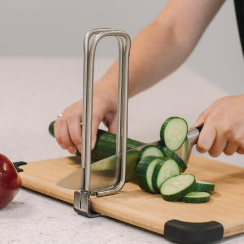A person chops cucumbers with a metal tool attached to the cutting board.
