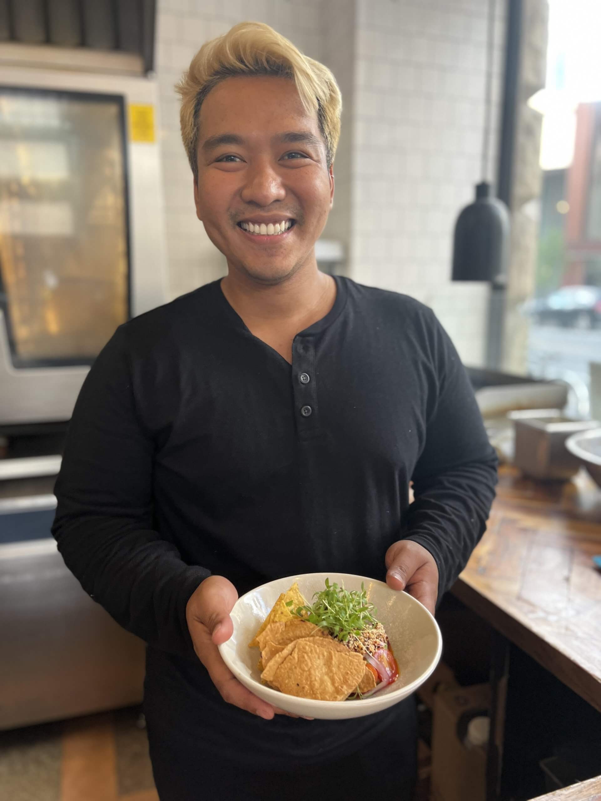 A man smiles while holding a bowl of food