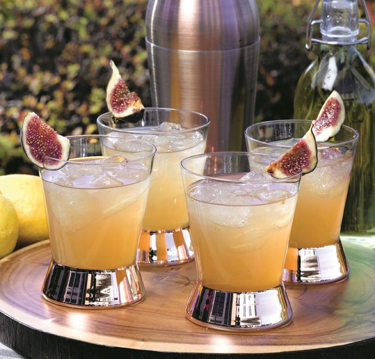 4 glasses with liquid and cocktail shaker outside on tray