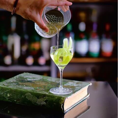 A cocktail is poured into a glass on top of a book