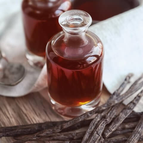 Glass bottles of vanilla extract with vanilla pods next to them
