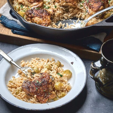 A black castiron pan with rice and chicken, a dish and a mug