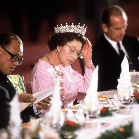 The queen adjusts her tiara at a banquet table