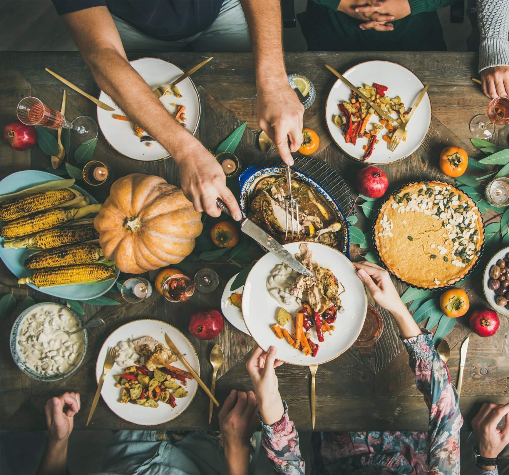 A wooden table topped with pie, pumpkins and plates of food.