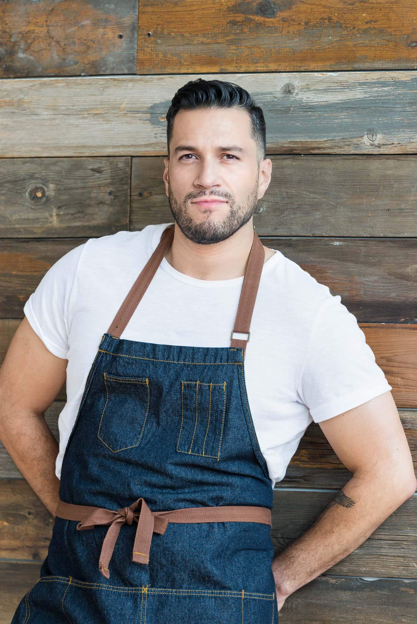 A chef in apron leans against wooden boards