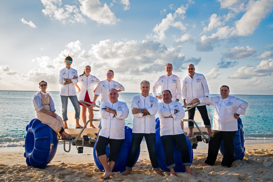 9 chefs wearing white chefs jackets on beach
