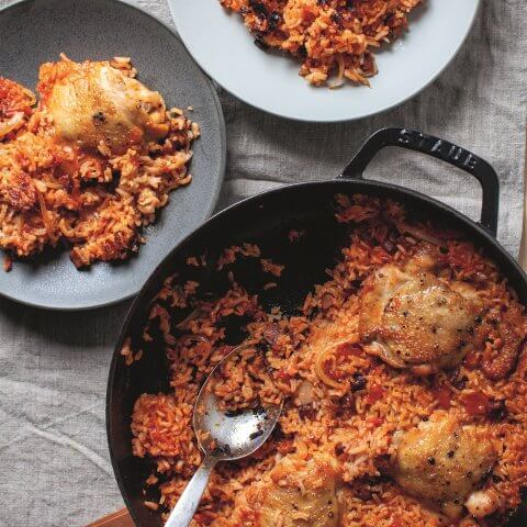 A pan and two plates with rice, chorizo and chicken thighs