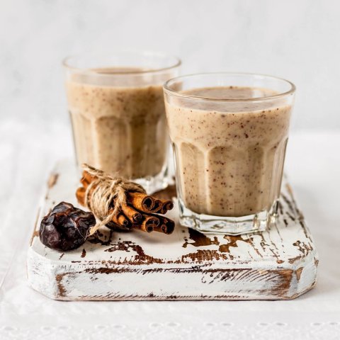 Two glasses of almond smoothie sitting on board