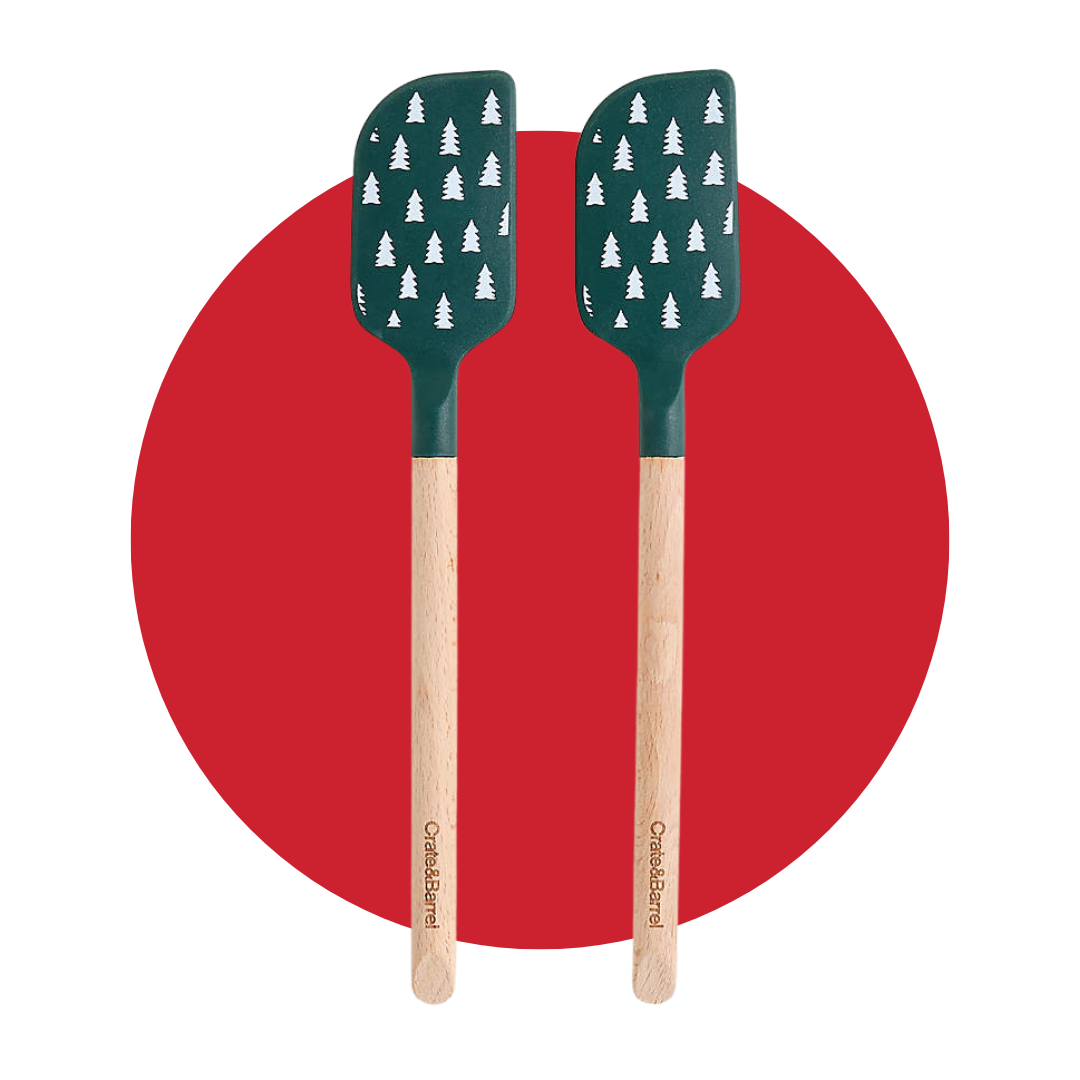 Two green spatulas with a white tree design and wooden handle on a decorative red circle background. 