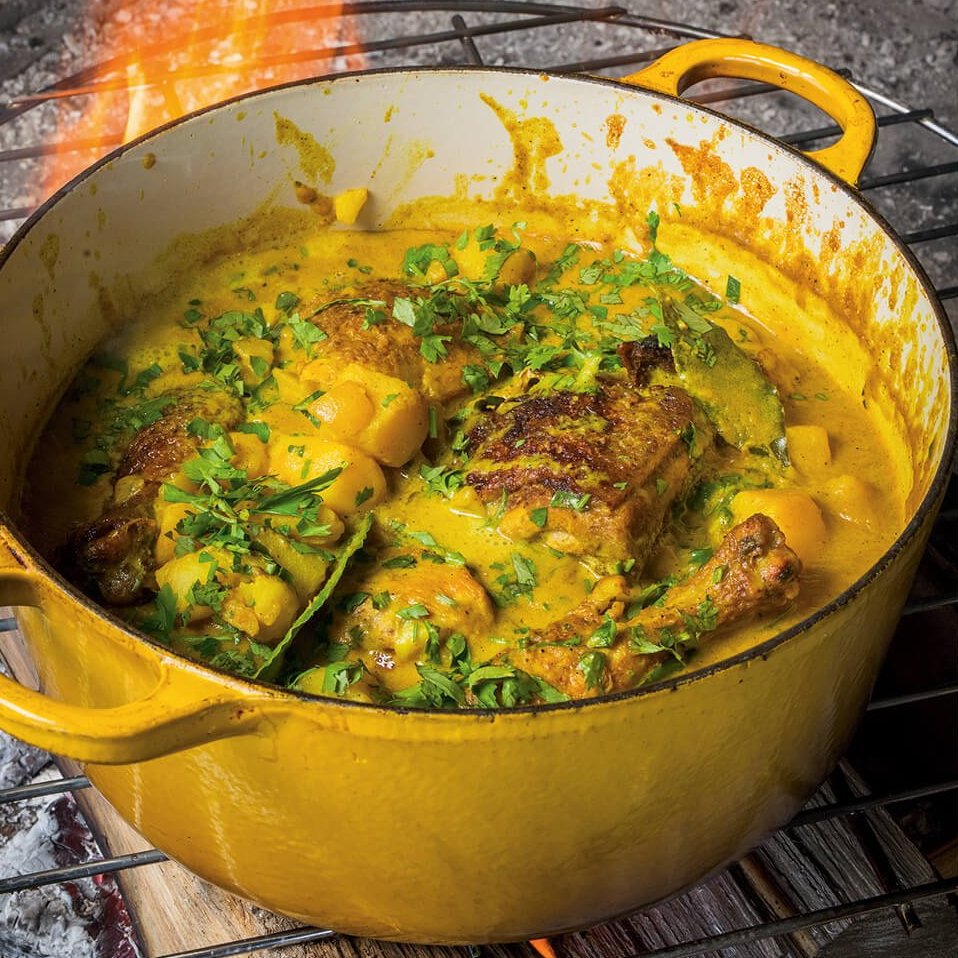 A yellow pot with curry chicken and flames in the background.
