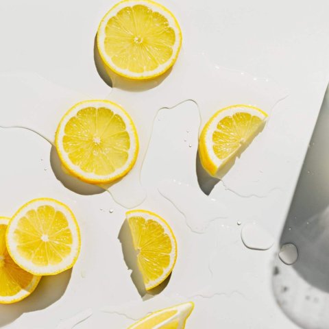 Fresh lemons cut into slices on bright white wet surface with gl