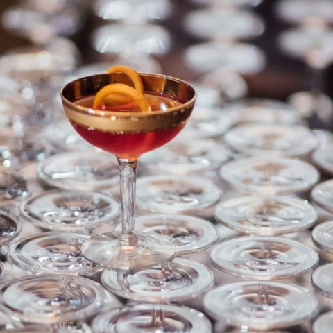 A coupe glass with orange rind and red cocktail on top of stacked glasses.