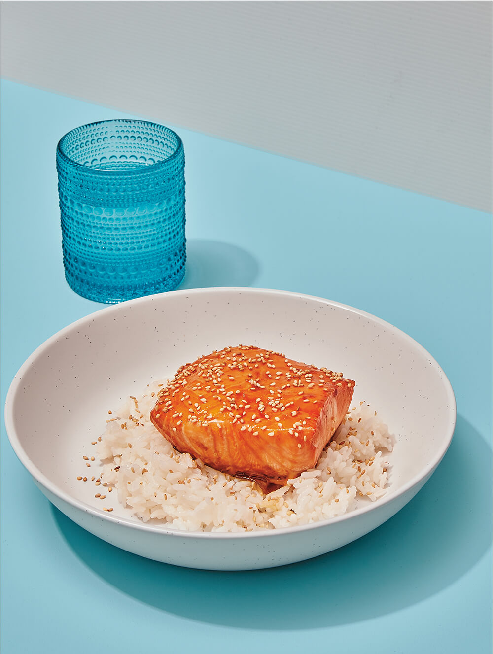 A dish with salmon on top of rice on a blue table with a blue glass.