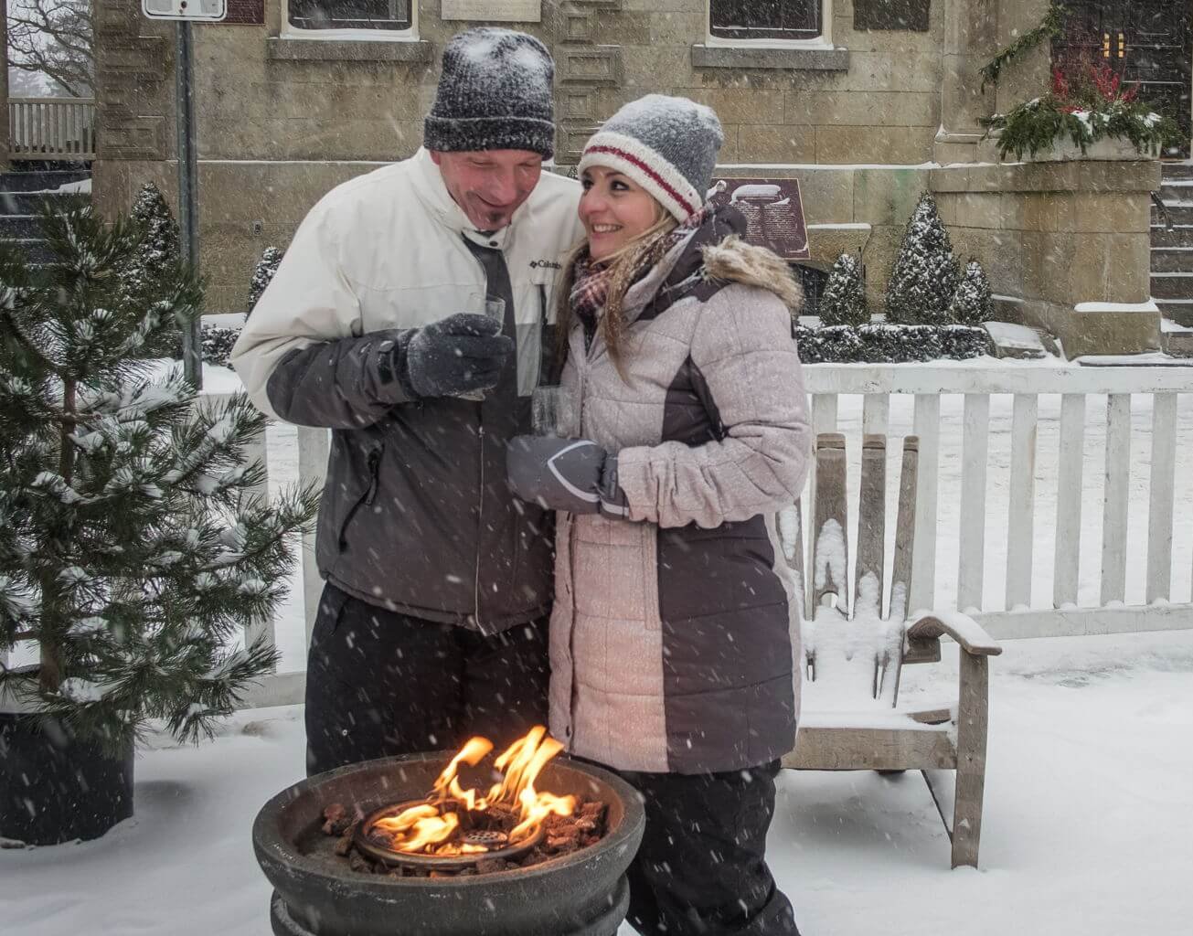 Man and woman in winter coats standing by firepit outdoors