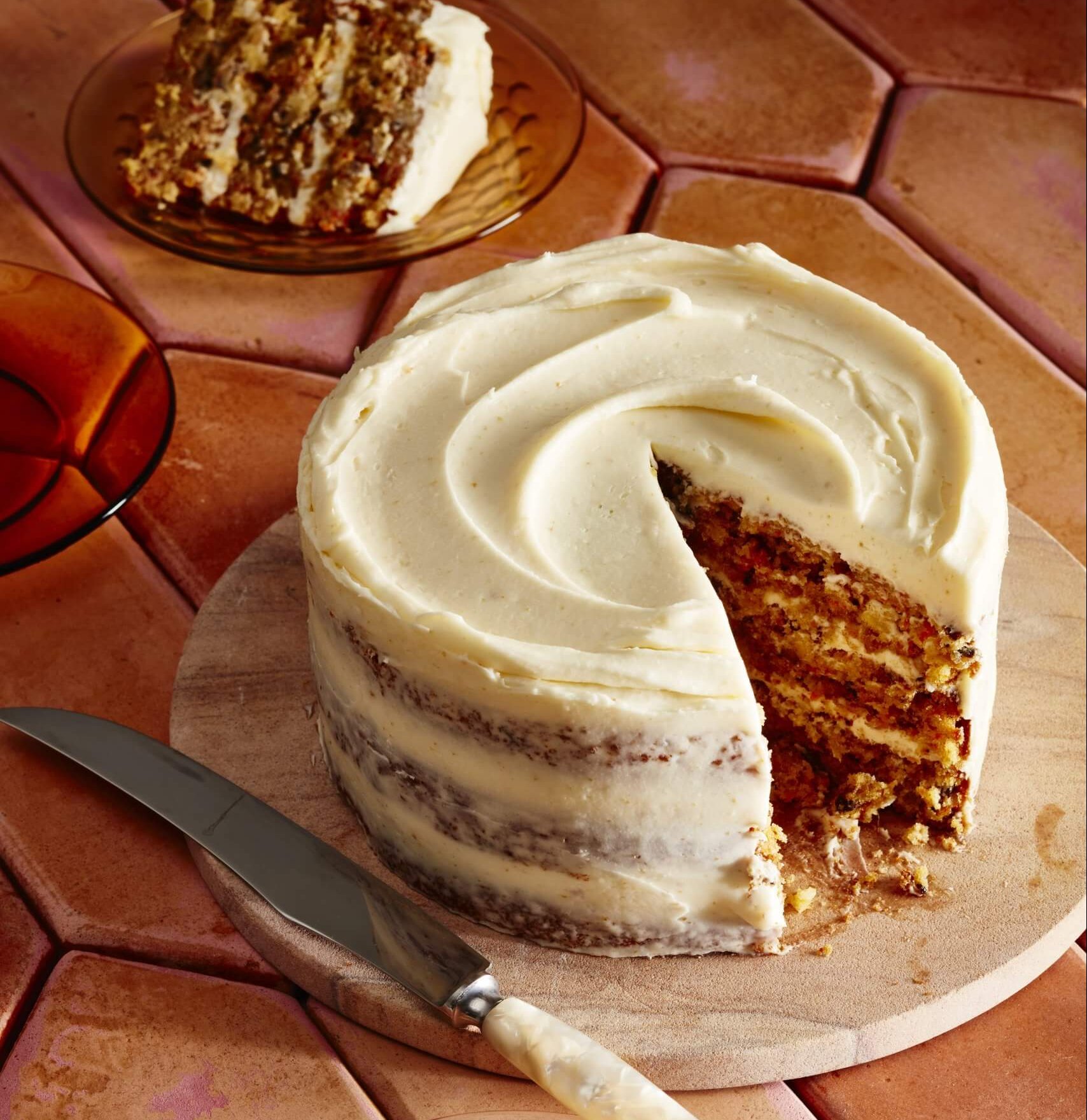 A carrot cake with white frosting and one slice cut out.