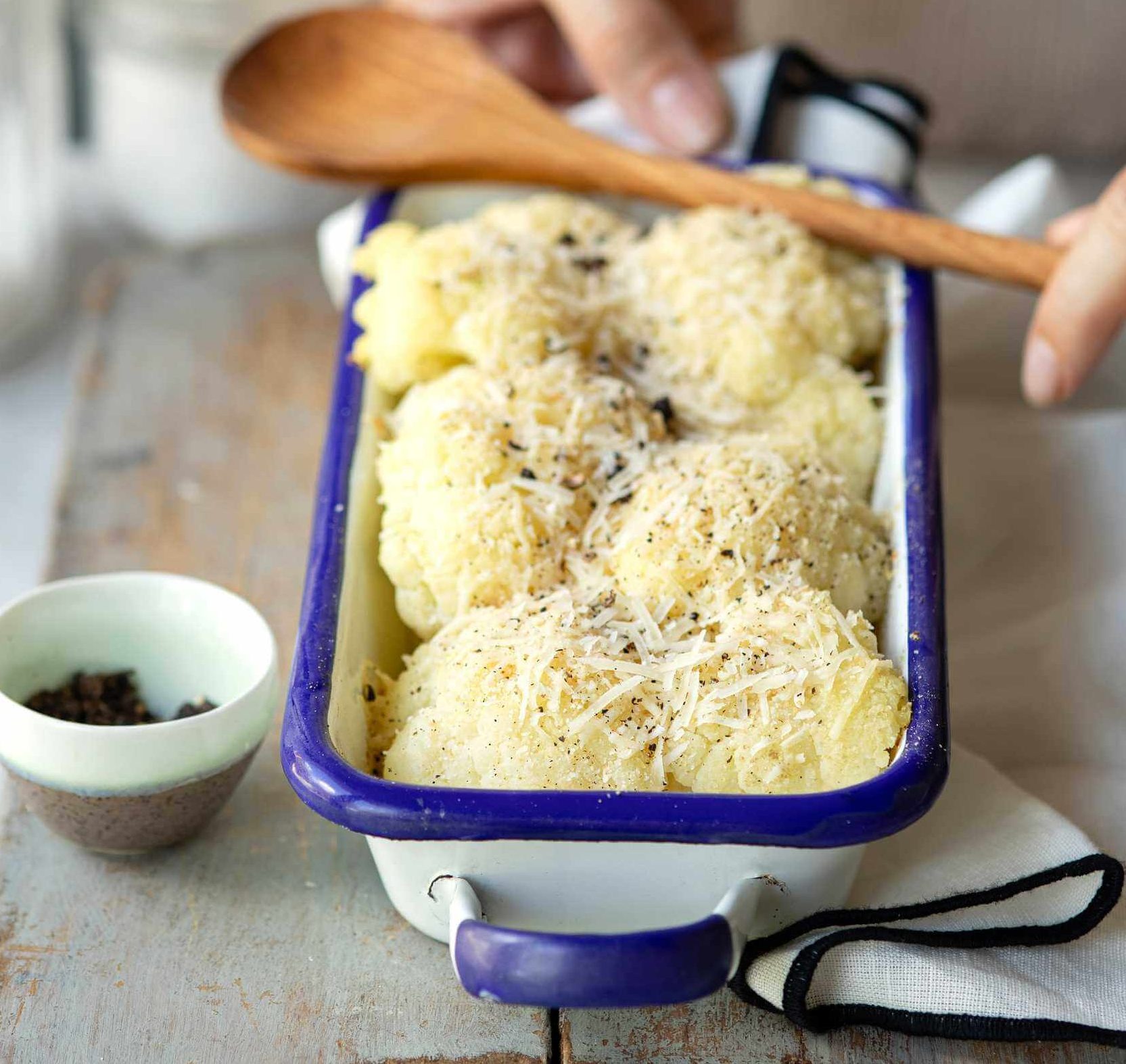 A person holding a baking dish with cauliflower and cheese.