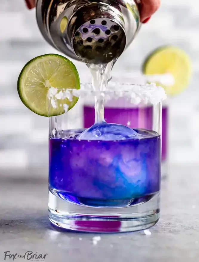 A cocktail is poured into a glass, turning bright purple.