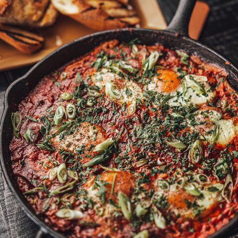 A skillet filled with shakshuka and sliced bread in the background.