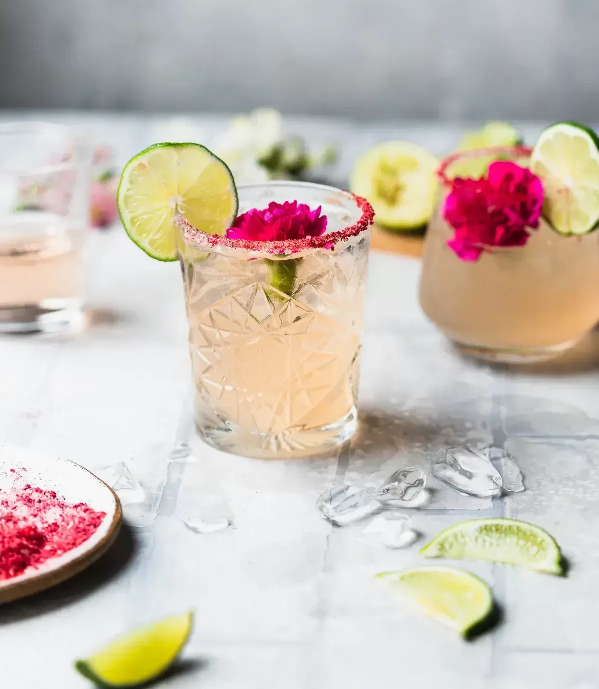 A tumbler glass with a cocktail garnished with lime and a flower.