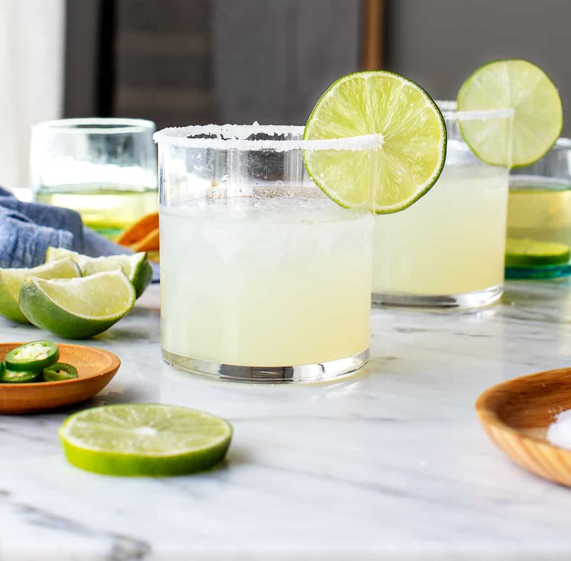 Glasses with Margaritas, salted rims and lime wedges on a countertop.