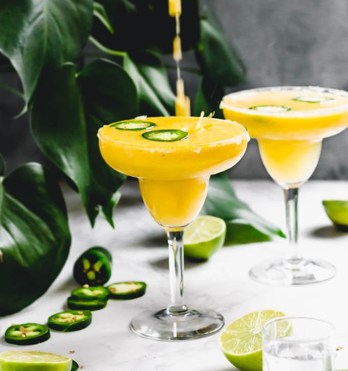 Two mango Margaritas with green leaves in the background.