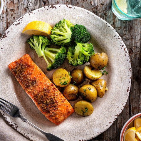 Overhead view of plate with salmon, lemon wedge, broccoli and pottoes