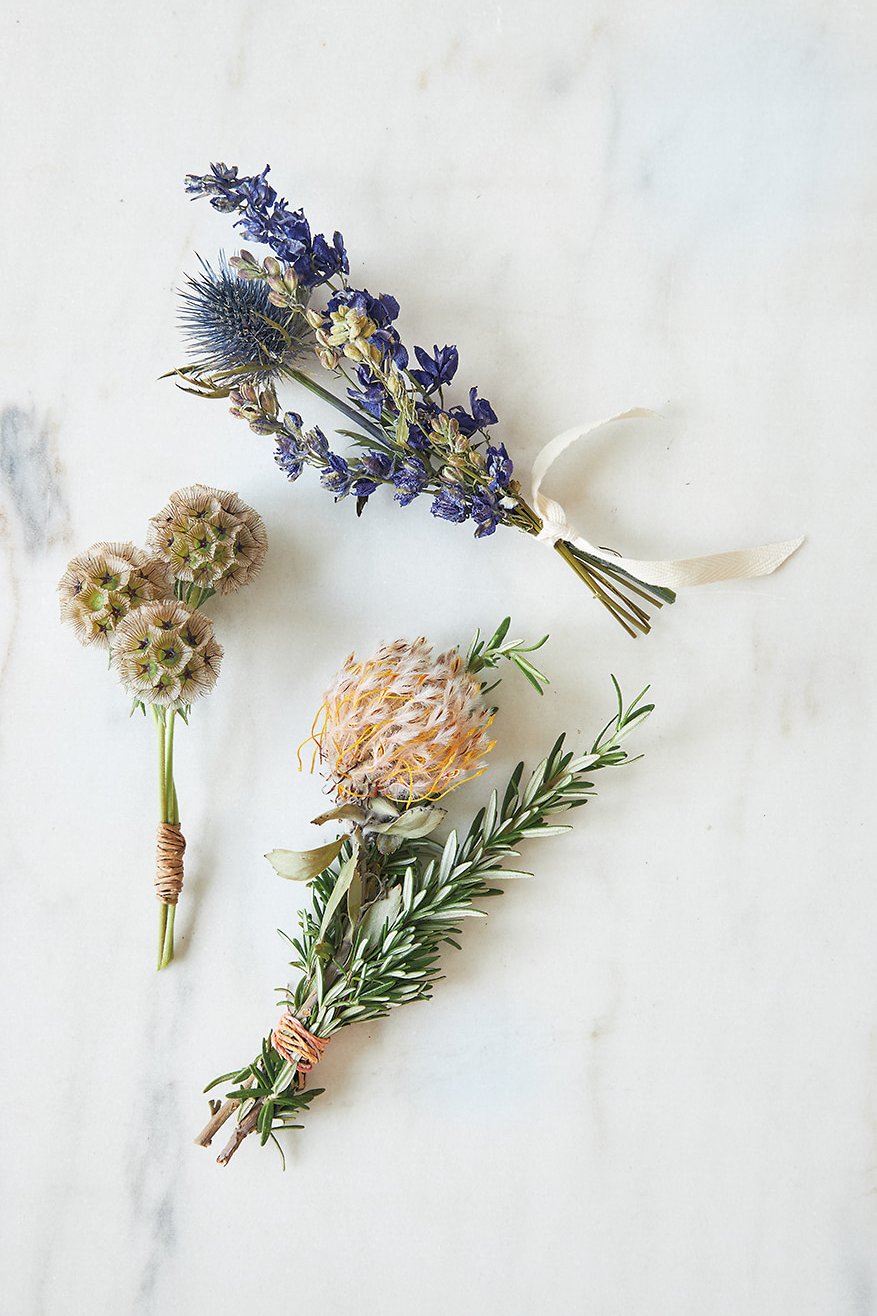 Three bundles of dried flowers on a white marble surface.