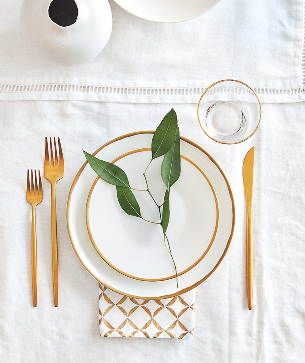 A white and gold place setting with eucalyptus leaves.