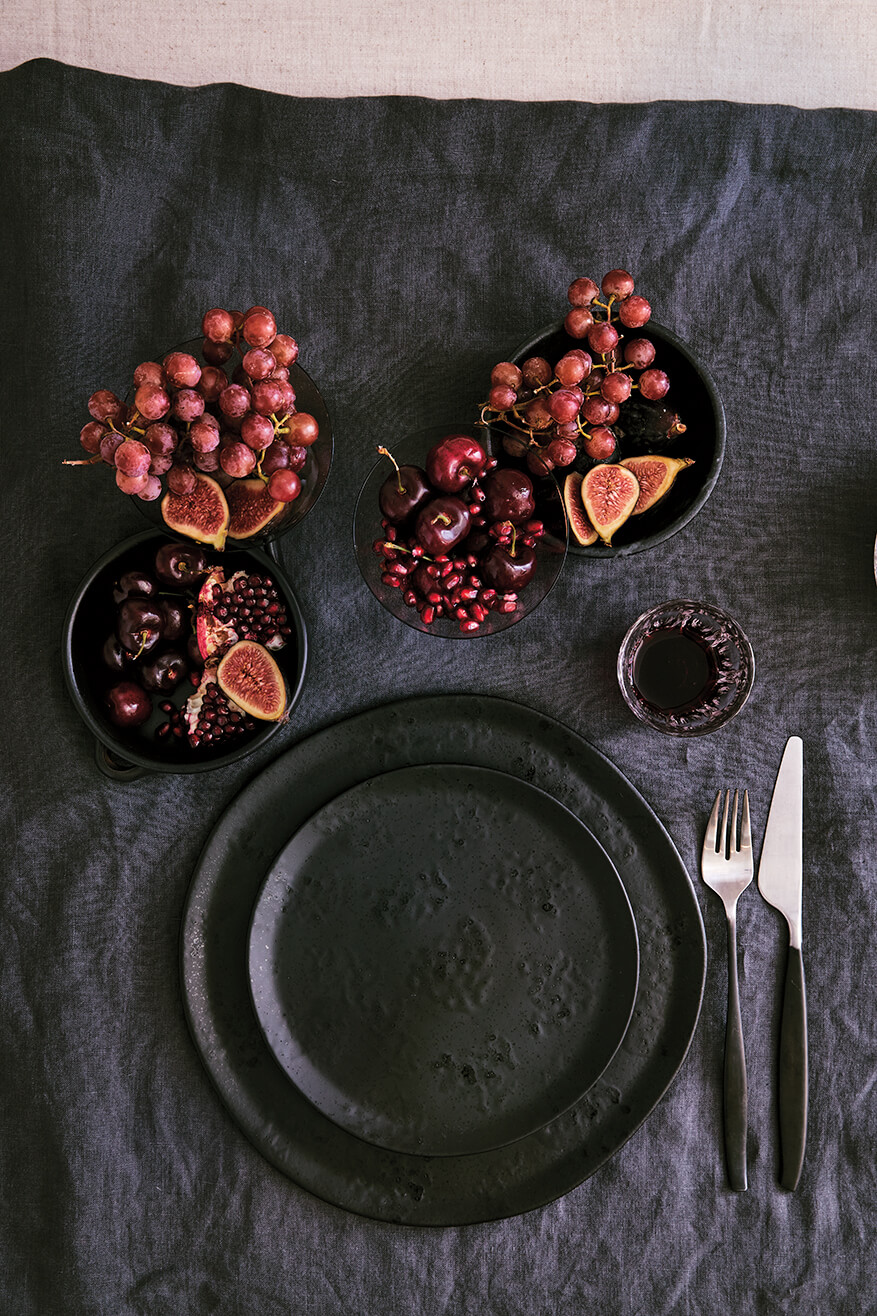 A black place setting with bowls of grapes and other fruit.