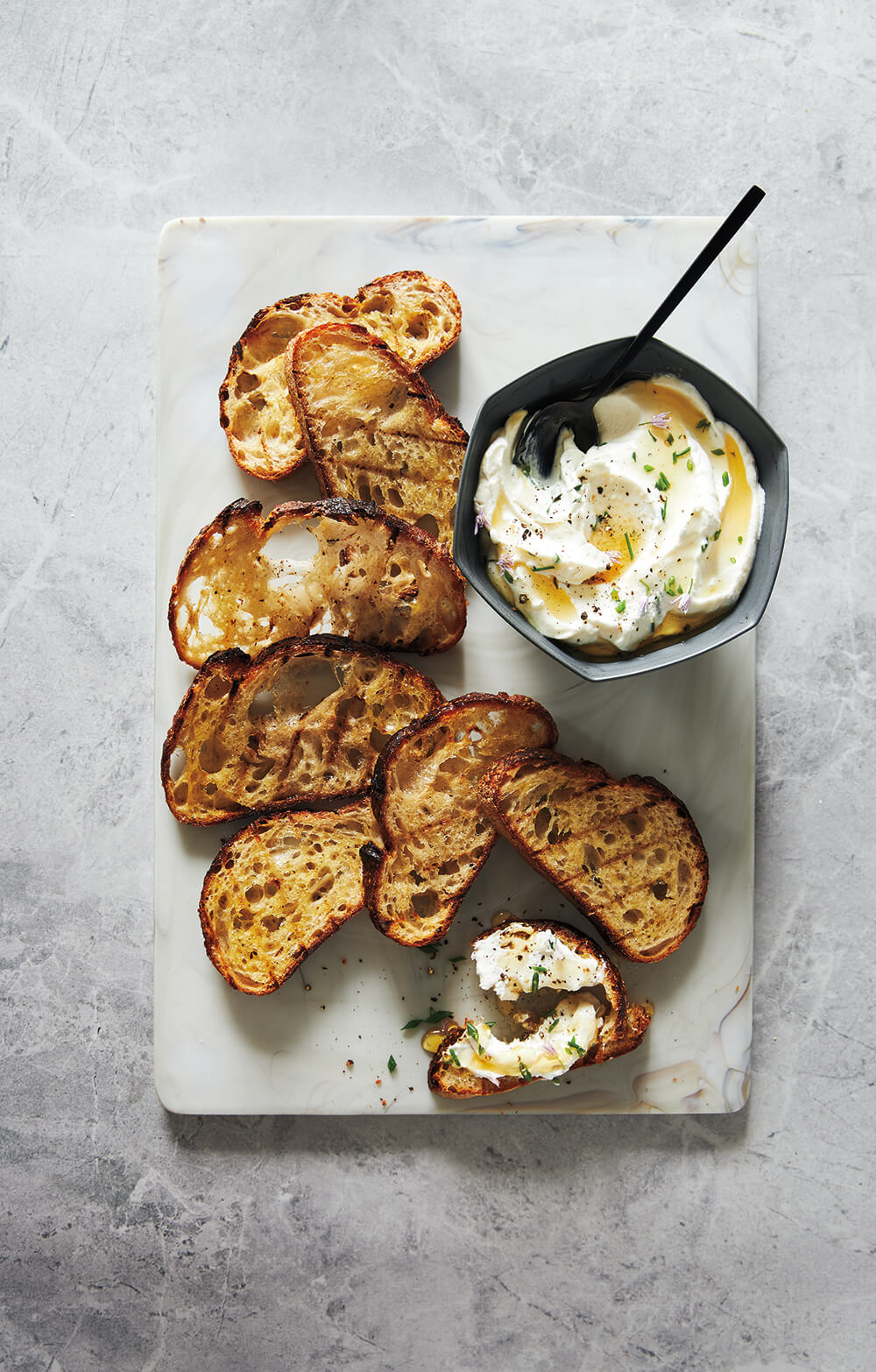 A stone surface with grilled bread and ricotta.