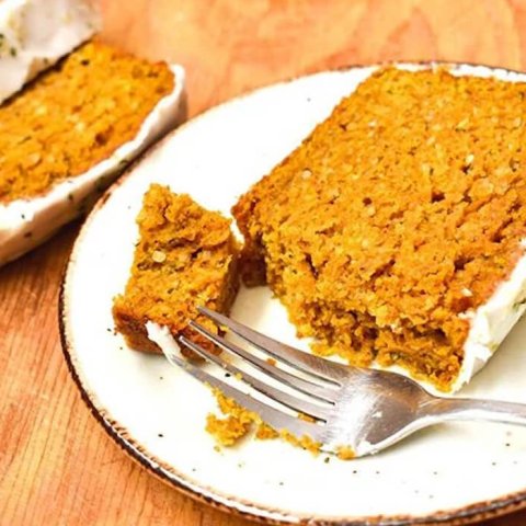 A sliced frosted pumpkin loaf and servings on white plates.