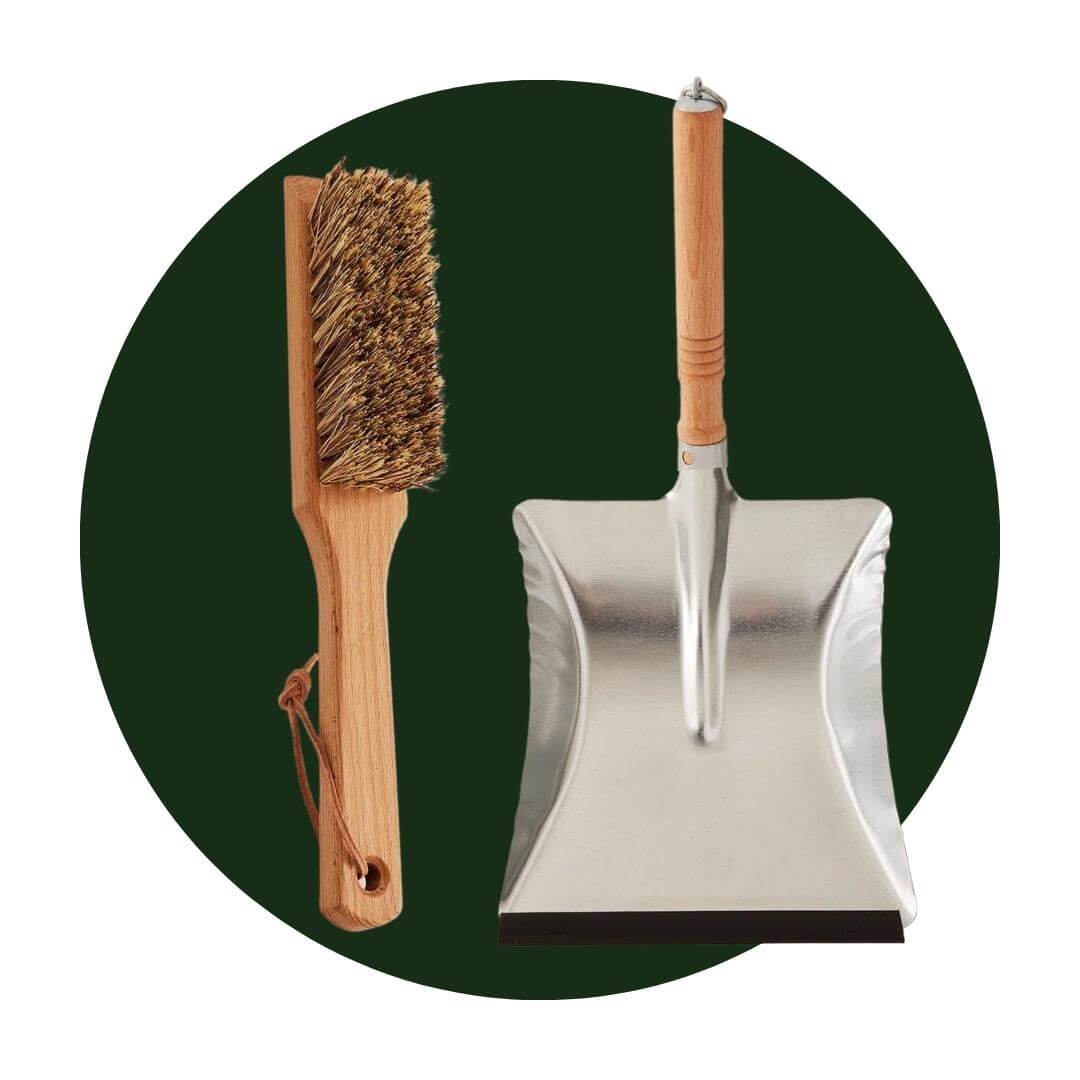 A wooden cleaning brush and metal dustpan on a dark green circle