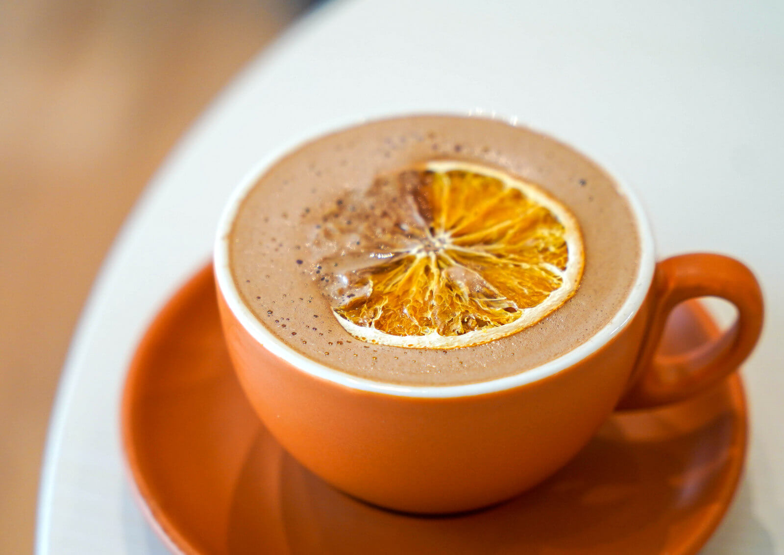 An orange mug of hot chocolate with a dried orange slice on top.
