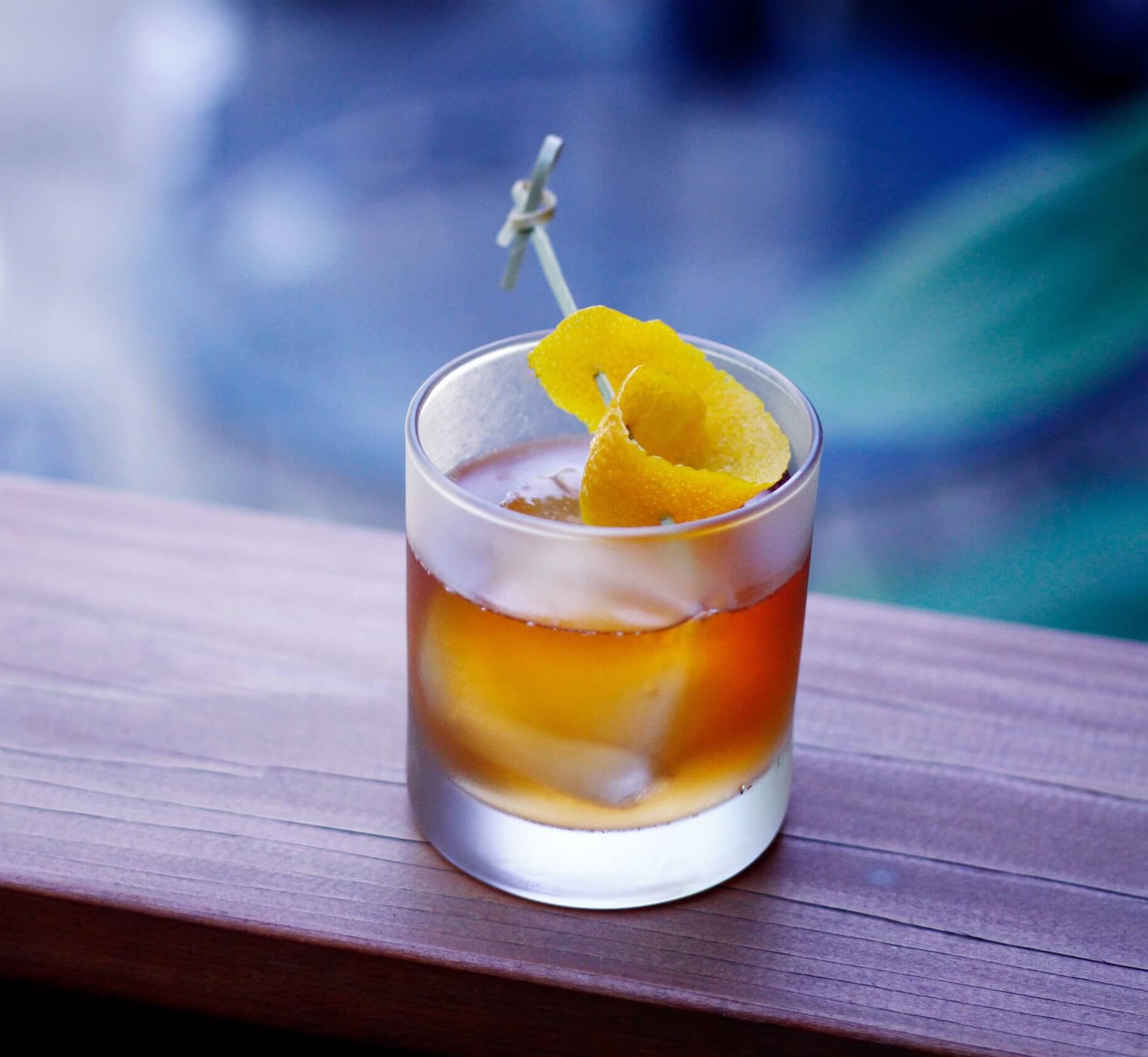 An old fashioned cocktail with an orange peel garnish on a wooden surface.