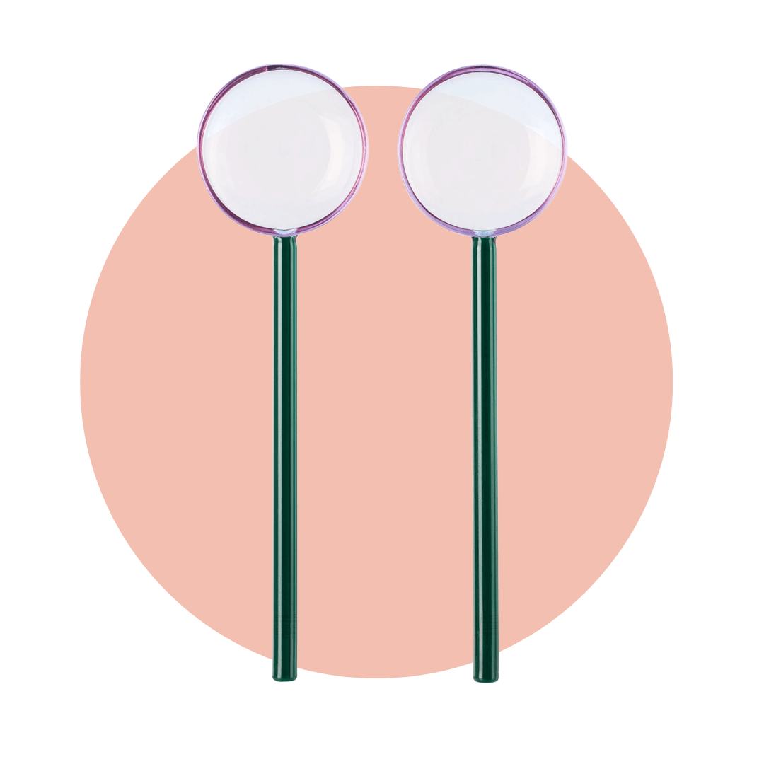 Two large salad serving spoons with purple glass bowls and dark green handles on a light pink circle background.
