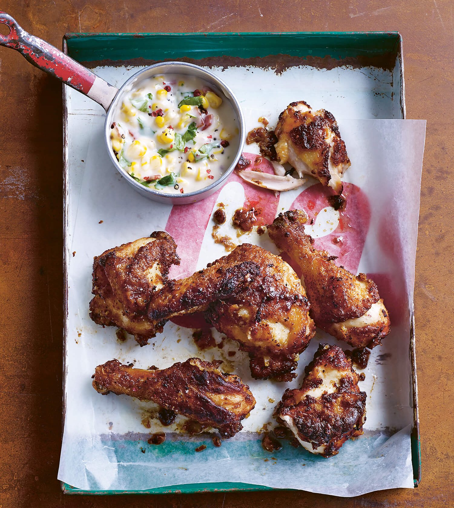 A tray with chicken wings and a side of creamed corn photographed from above