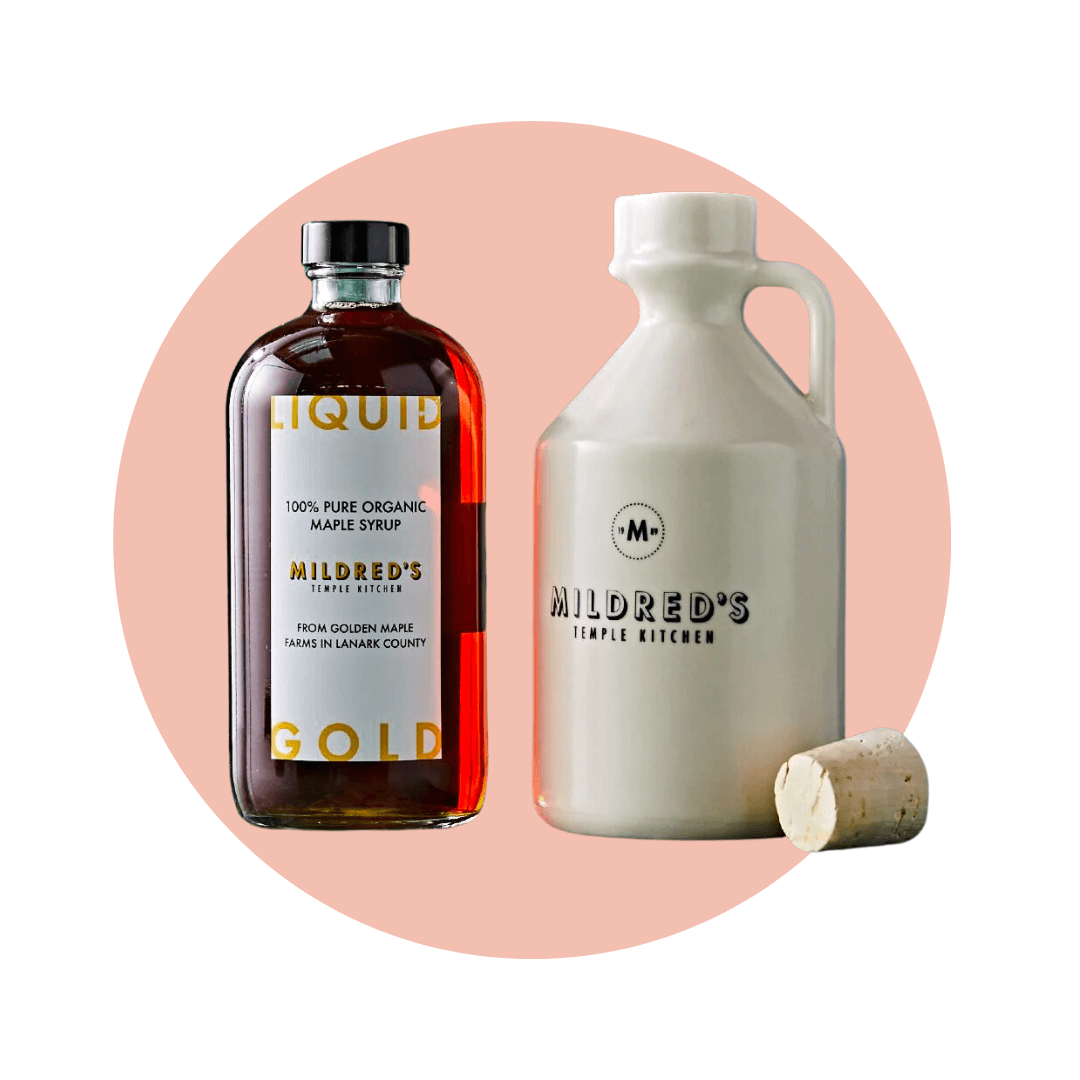 A bottle of maple syrup and a white ceramic jug with cork on a light pink circle graphic.