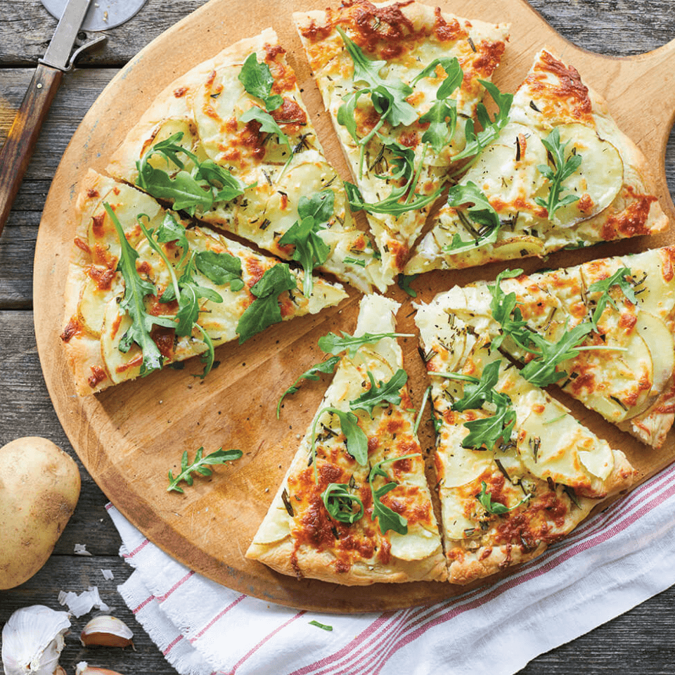 A pizza on a wooden tray with potatoes next to it.